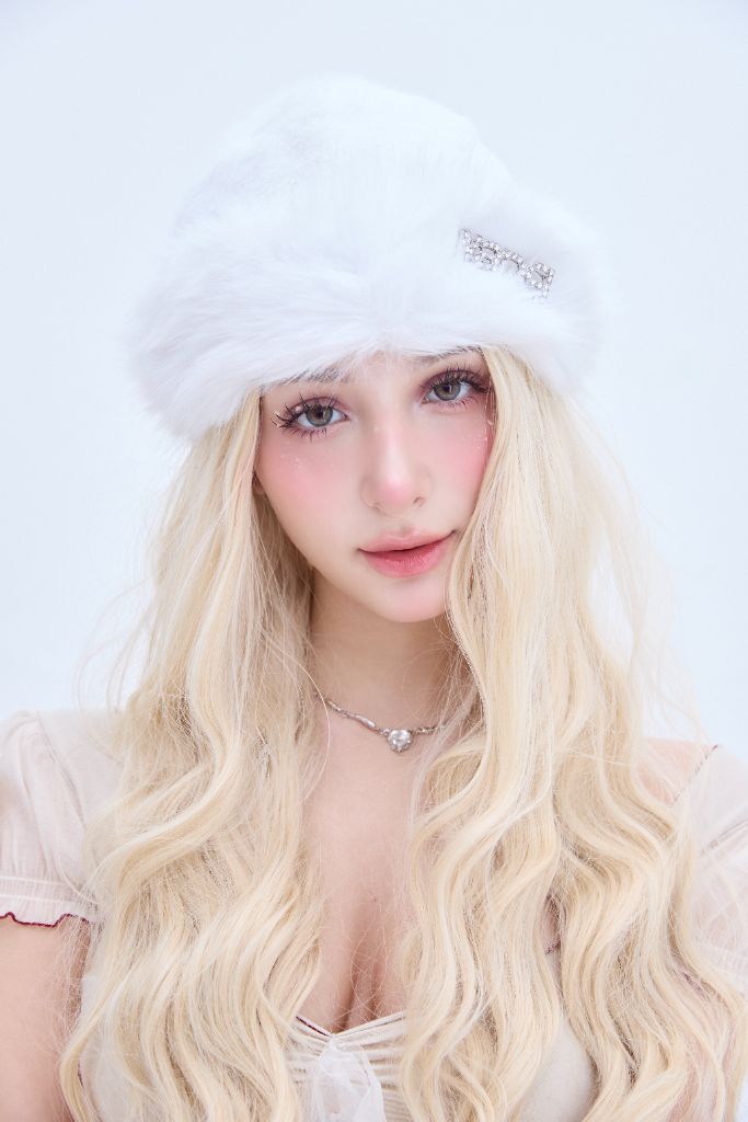 Person mit langen blonden Haaren, die einen weißen Hut trägt, vor weißem Hintergrund